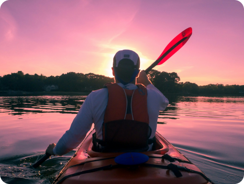 Over the shoulder picture of the owner in a kayak during a beautiful pink and yellow dusk